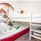 A white loft bed with a bed underneath with stuffed animals on it and painted mushrooms on the wall.