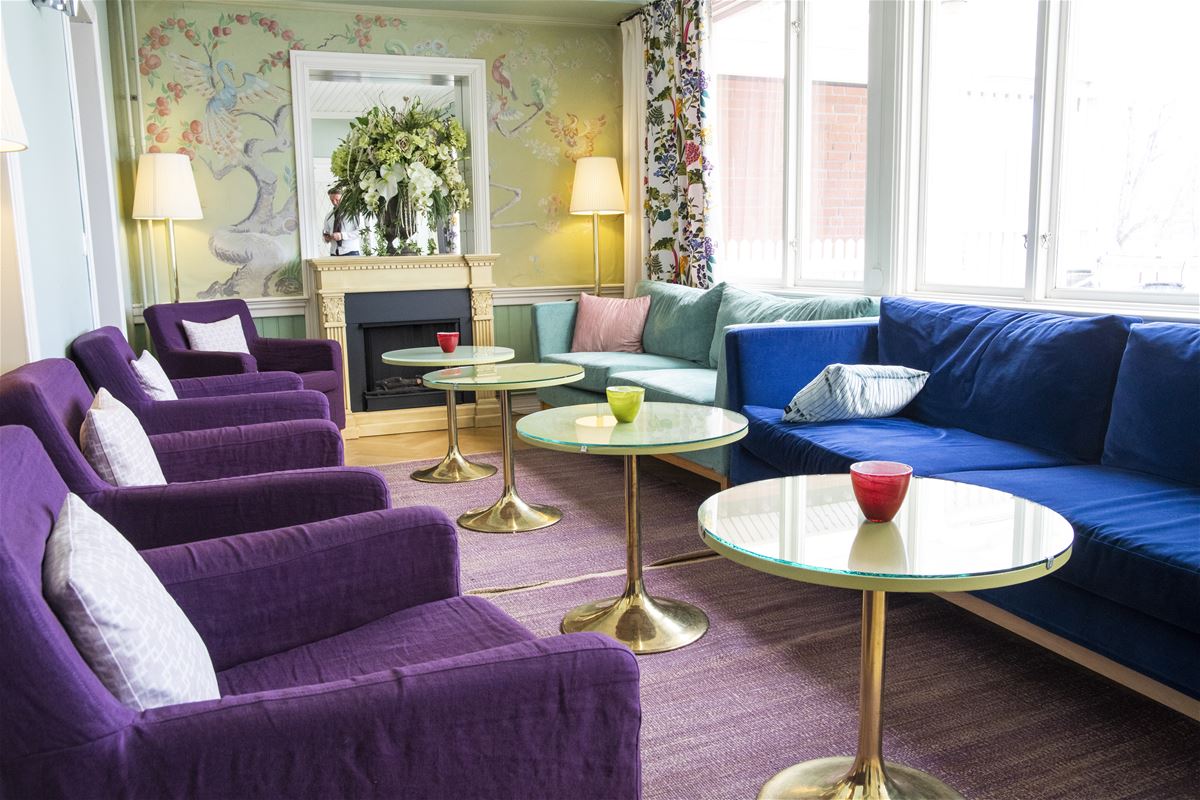 En blå soffa och flera lila fåtöljer och runda pelarbord i lobbyn. 