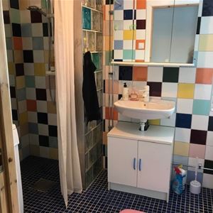 Badrum med dusch, handfat och toalett med färgglada kakelplattor på väggarna.