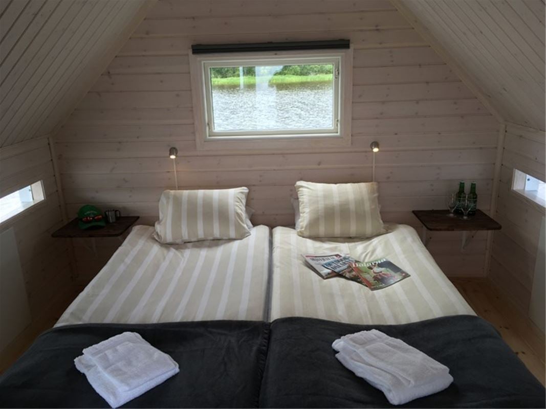 Dubbelsäng med litet fönster ovanför sängen och brädklädda väggar.