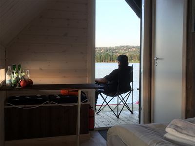 Utsikt genom dörröppning ut mot vattnet och en altan med siluett på en person i en stol.