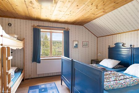 Sovrum med blå dubbelsäng och en våningssäng i furu, fönster med utsikt. 