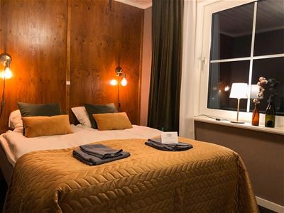 Double bed with lit bedside lamps on the wall behind.