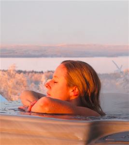 Woman relaxing in the jacuzzi with frost-covered trees and Siljan in the background.