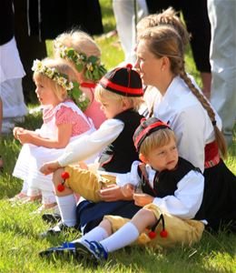 Children in folklore costume and flower wreaths in their hair are sitting on the lawn. 