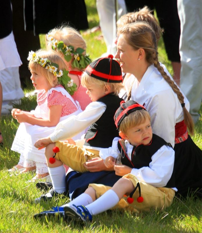 Children in folklore costume and flower wreaths in their hair are sitting on the lawn. 