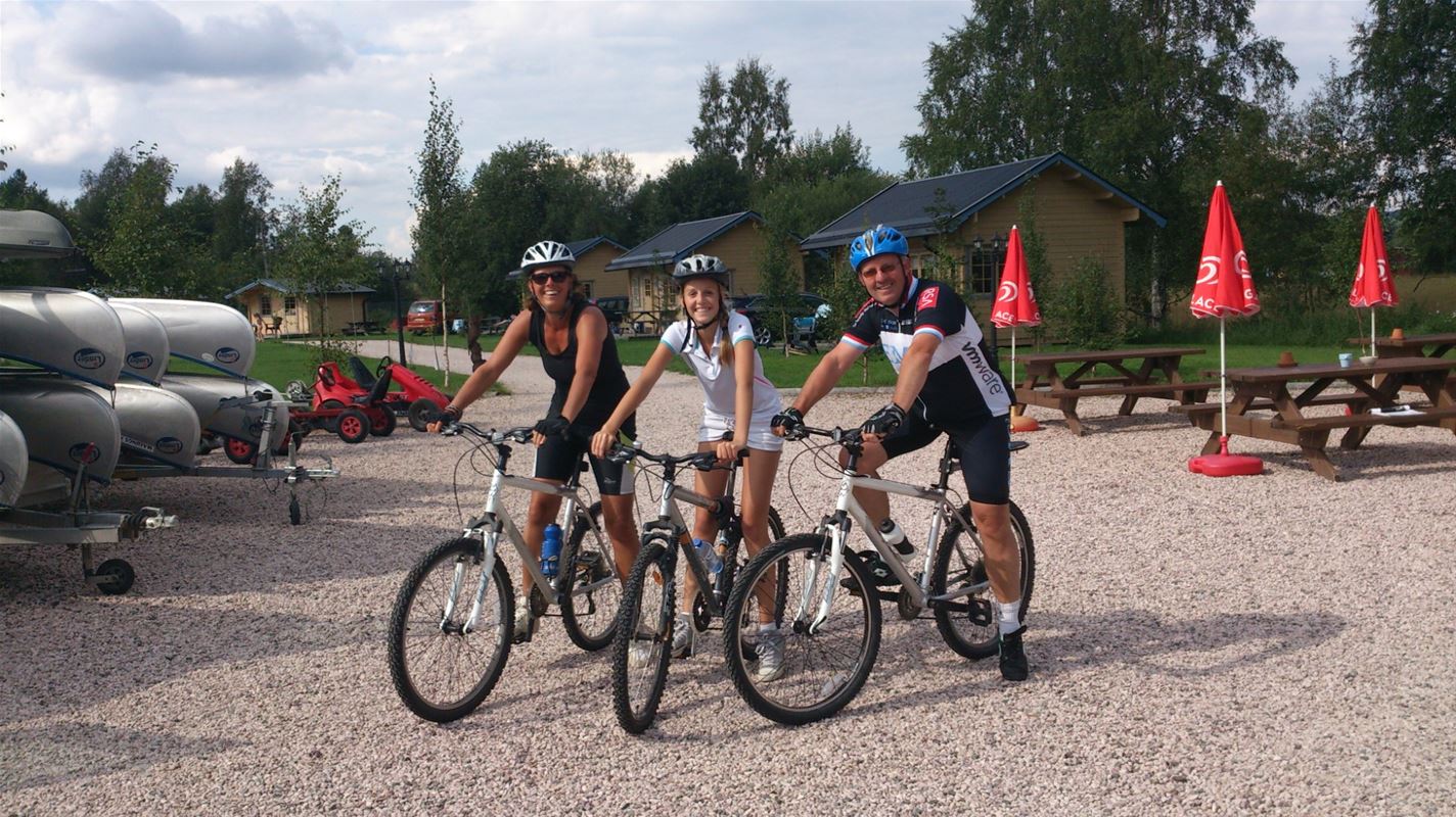 Tre cyklister på en grusad parkering. 