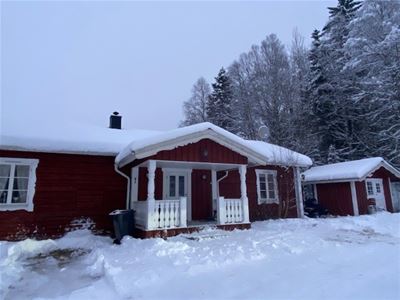 Timber cottage with white windows and snow on the roof and on the ground. 