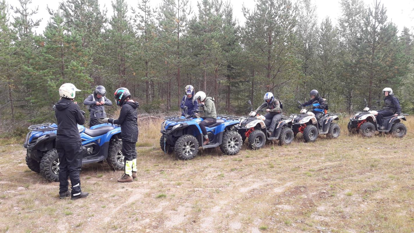 Några personer med fyrhjulingar står på rad längs skogsbrynet. 