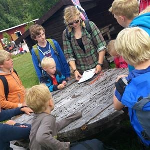 Några barn som står samlade runt ett bord av trä och lyssnar på en ledare. 