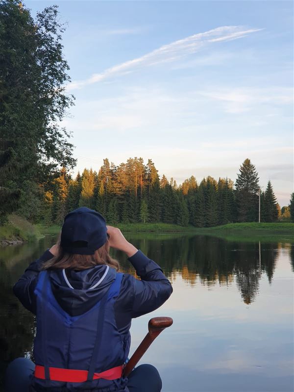 A person is sitting in a canoe and looking through binoculars.
