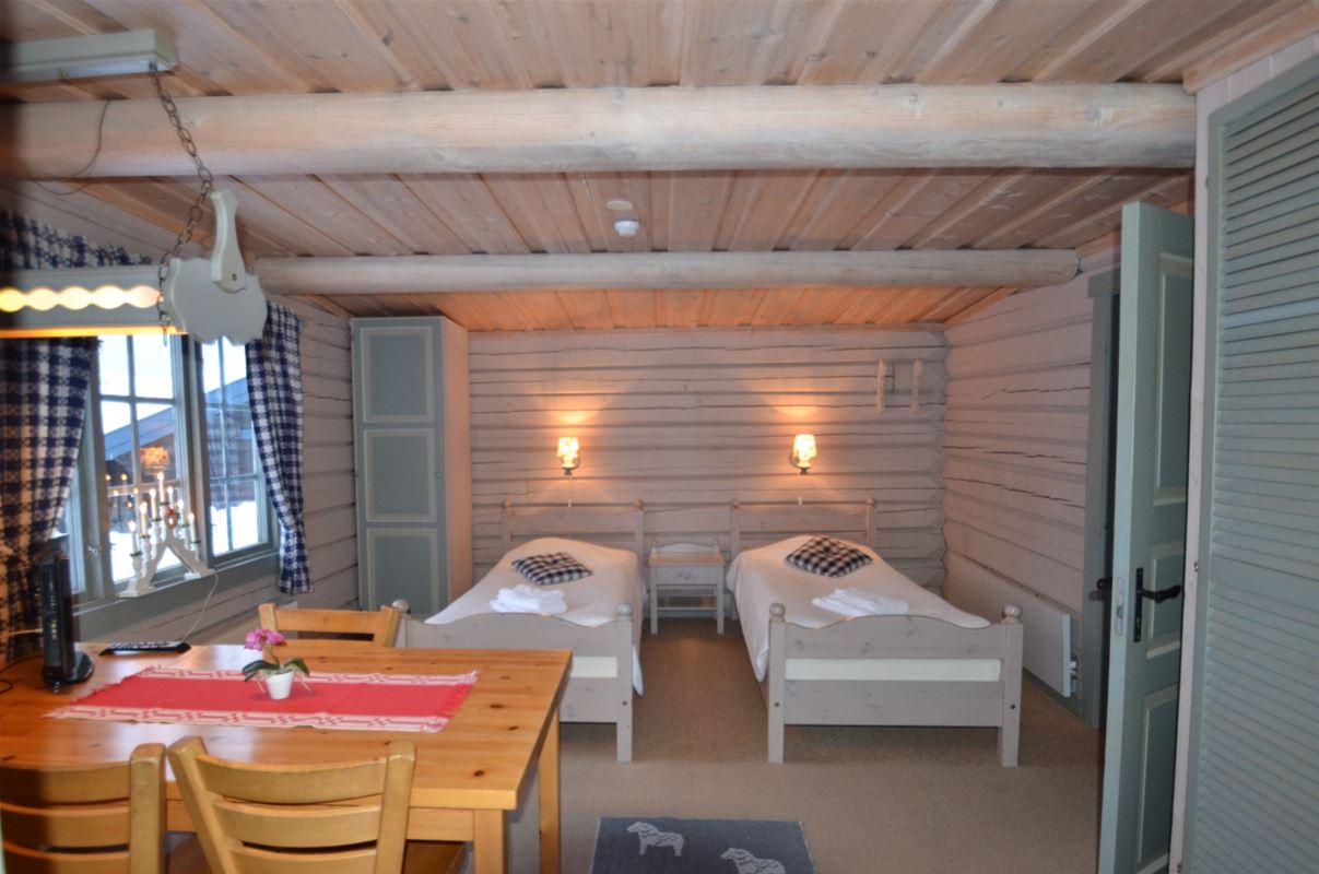 Two single beds placed against a white, painted timberwall and dining furniture in pine. 