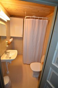 Bathroom with yellow walls, shower wit white curtains, toilet and handbasin. 