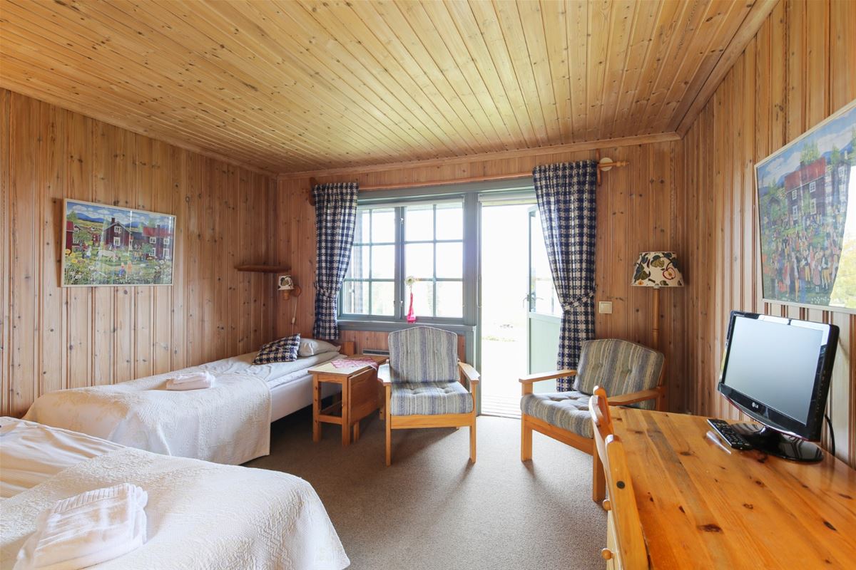 Two single beds placed in an angle to each other and two wooden armchairs in front of an open balcony door.