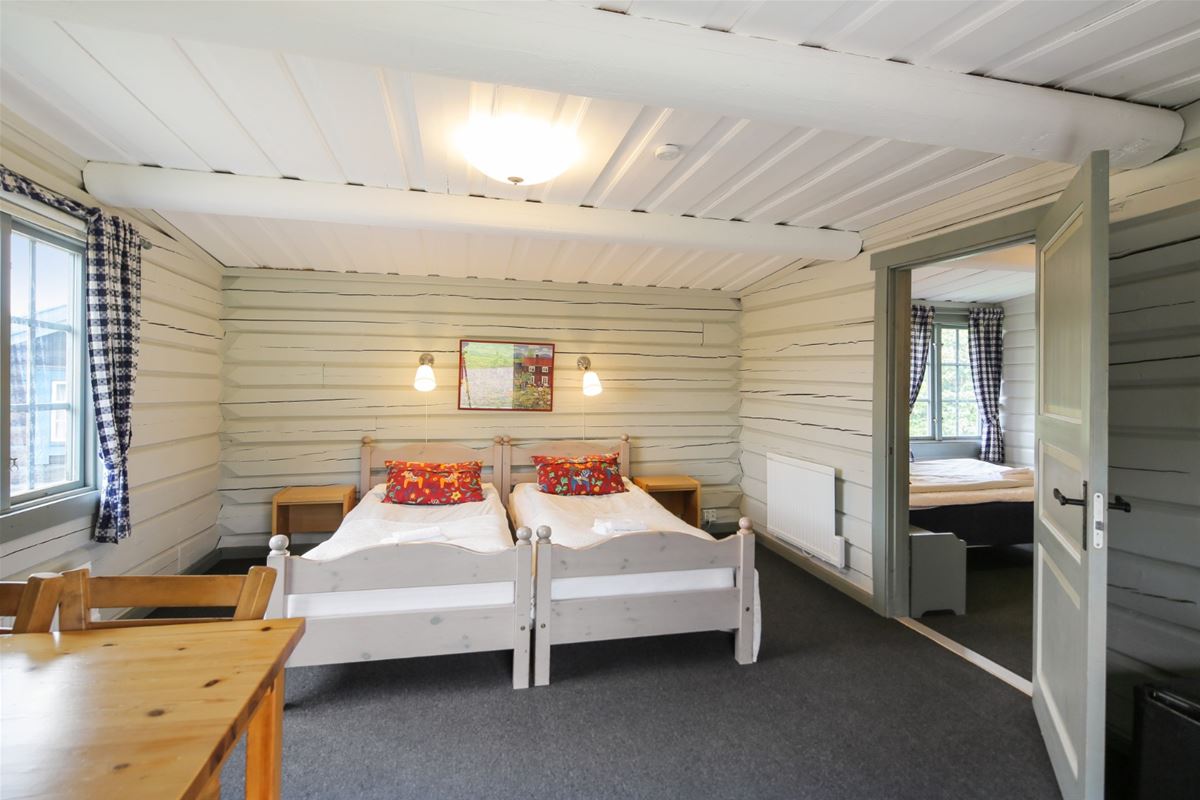 Two single beds with white bedspread and red pillows put together in front of white timbered walls. 