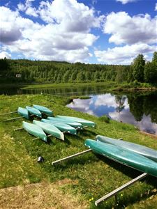 Flera kanoter ligger upplagda på gräset bredvid vatten. 