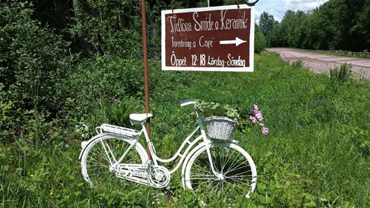 A white women's bicycle in the grass, sign Tidlösa smide & keramik.