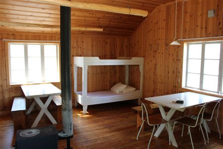 Room with a bunk bed, two dining tables and a fire place.