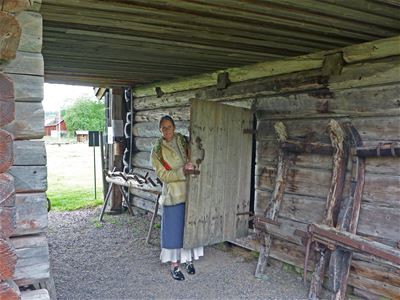 Woman looking forward behind door in old log house.