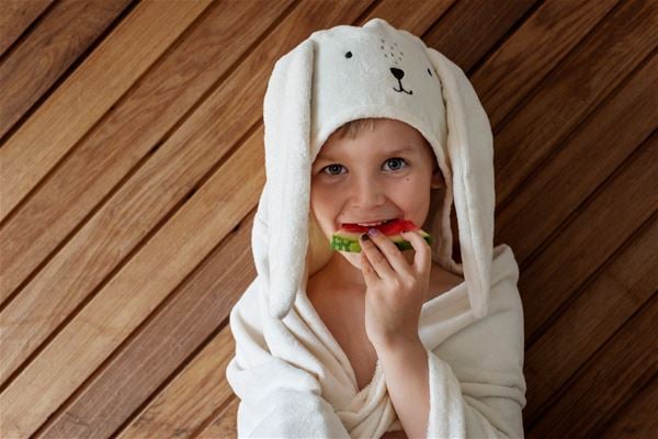 Ett barn i badrock som äter melon.  