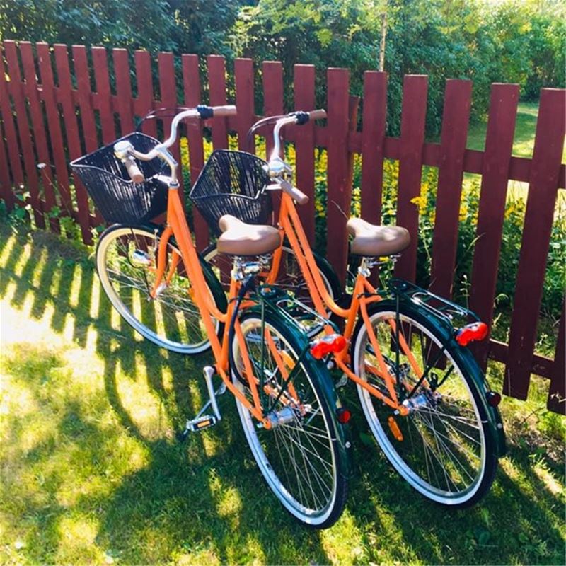 Two orange bicycles by a red fence.