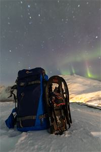 Sekk og truger på et snødekt fjell med nordlys bak