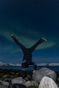 man doing somersault on the rocks under northern lights