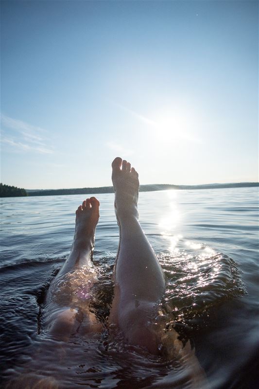 Fötter  i vatten i solnedgång.