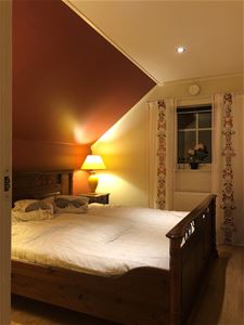 A double bed with white linens and a lamp that shines on a bedside table.