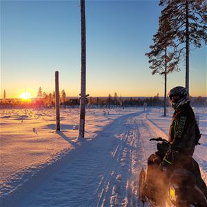 A man on a snowmobile looking at the sunset.