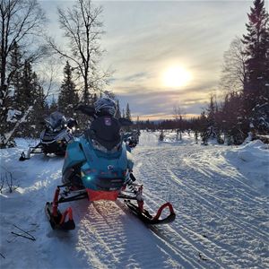 Two snowmobiles with a sunset.