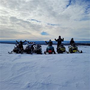 Six persons on their parked snowmobiles. 