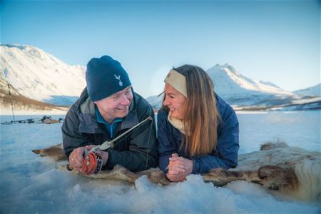 a couple laying on reindeer hides while ice fishing