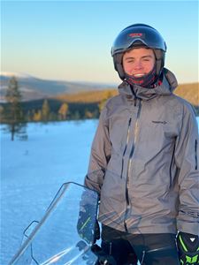 Kille med hjälm står vid en skoter på fjället. 