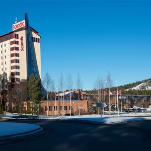 A tall bright building, red details and glass sections, ski jumps in the background.
