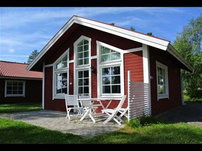 Röd stuga med stora fönster och uteplats med möbler.