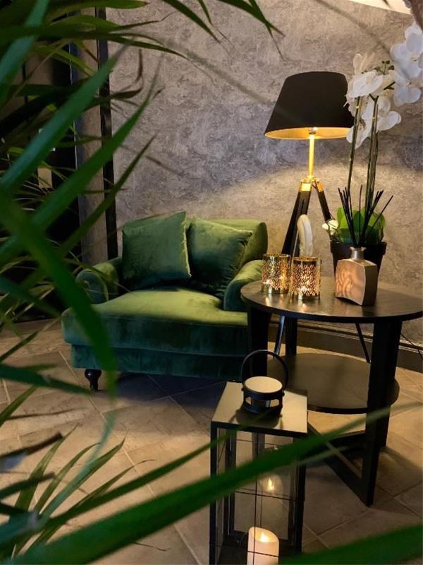 Fåtölj intill ett runt bord med en orkidé och lampa.