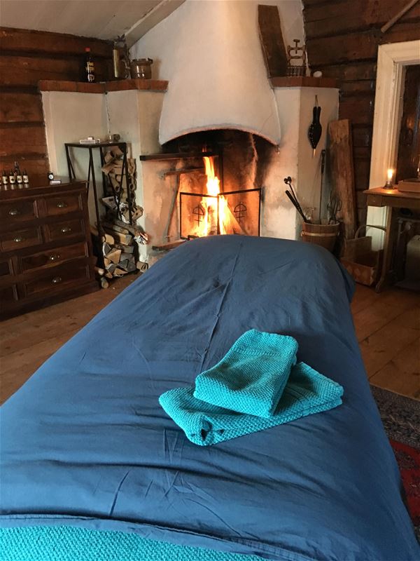 A bed with two towels on top, a open fire in the background.