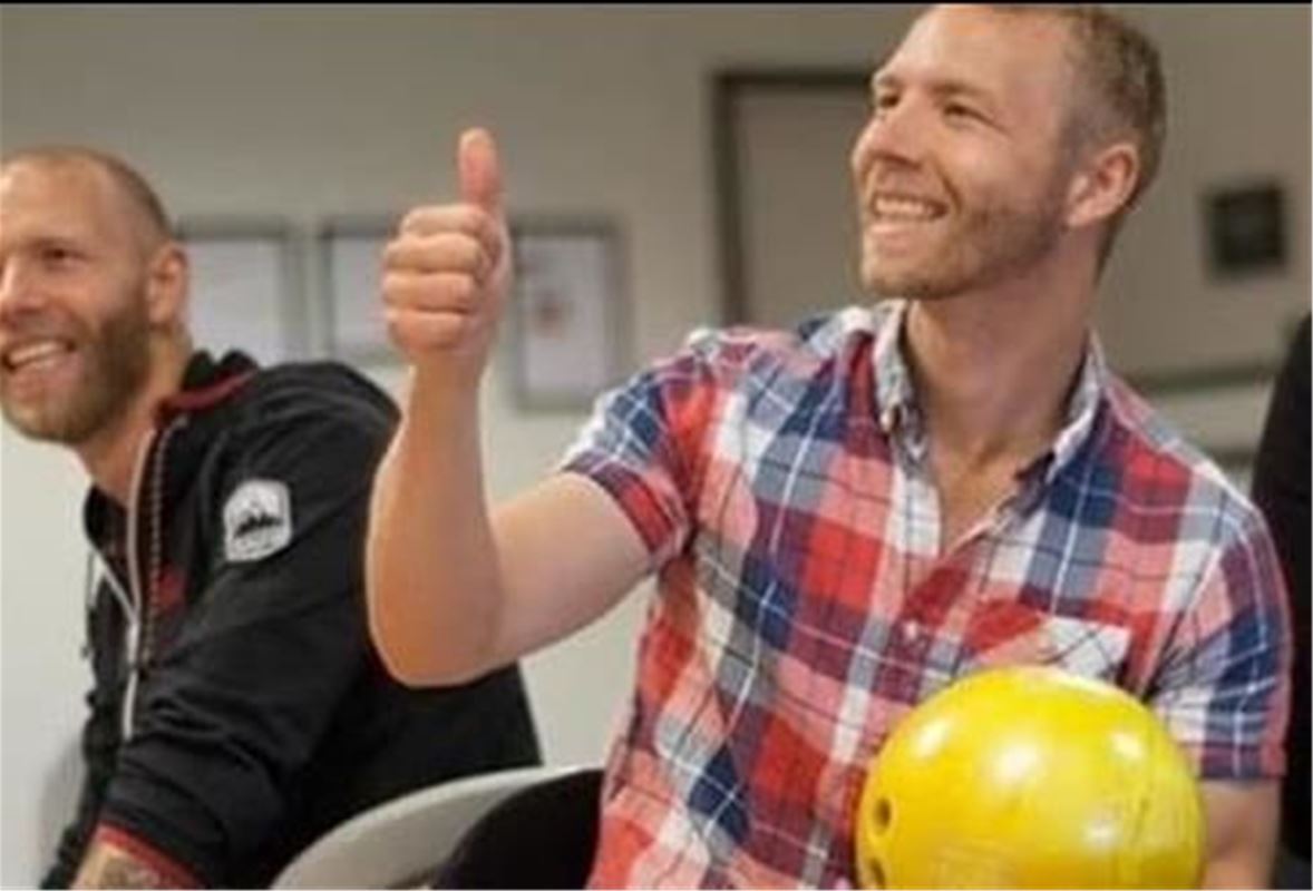 En glad kille med gult bowlingklot i handen och tummen upp.