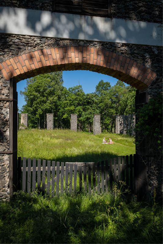 En portal i slaggsten med en trägrind, en familj som har picknick i gröngräset, slaggstenspelare i bakgrunden.