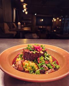 En tallrik med en köttbit, och tillbehör som står på en disk, i bakgrunden en restaurang.