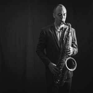 En svartvit bild på en man i kostym som spelar saxofon.