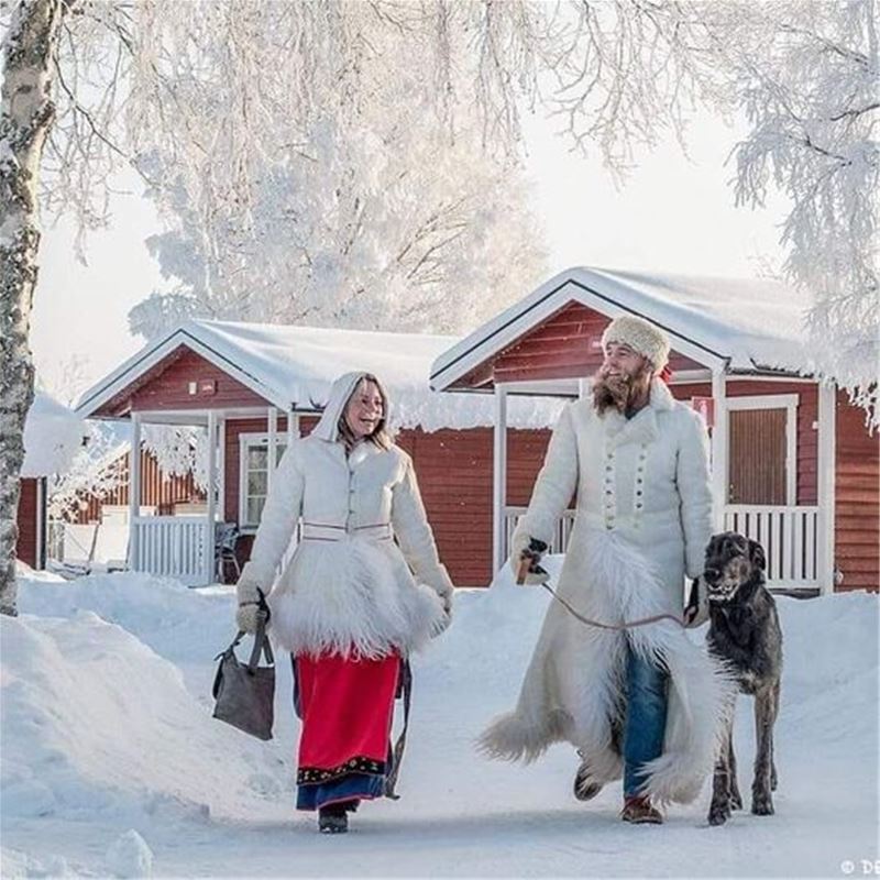 A couple in Malung's winter folk costume and the man have a large dog on a leash.