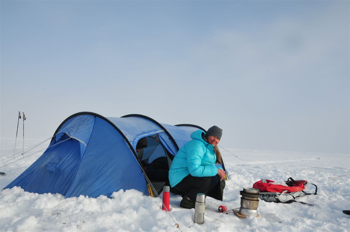 En campande dam som sitter vid sitt tält på ett snöigt fjäll.
