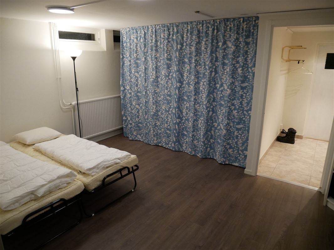 Two single beds in a room with white walls and a bue patterned curtain covering an opening in the wall.