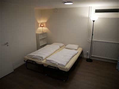 Två resesängar i ett rum med vita väggar och mörkt golv.