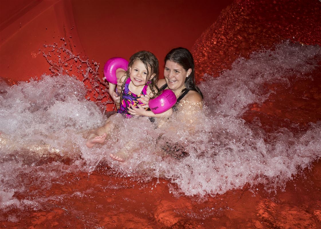 En kvinna och en liten tjej som åker i en röd vattenrutschkana.