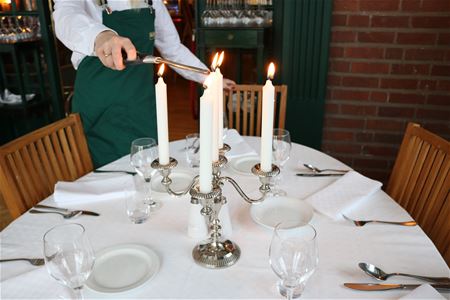 Someone lights a candelabrum at a set table.