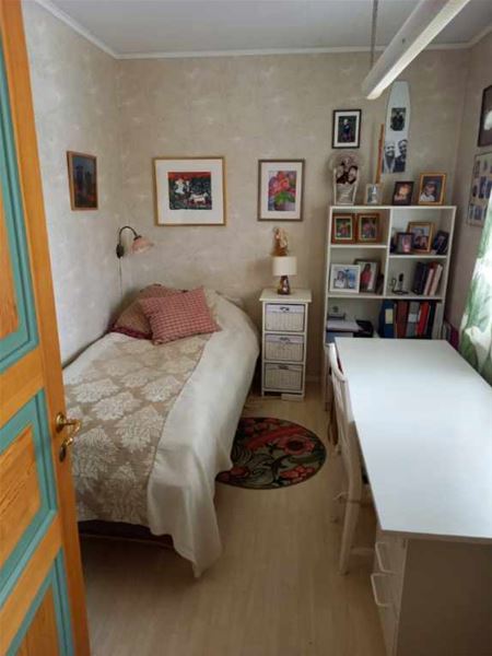 Litet rum med en enkelsäng, ett skrivbord vid fönstret och en bokhylla. 