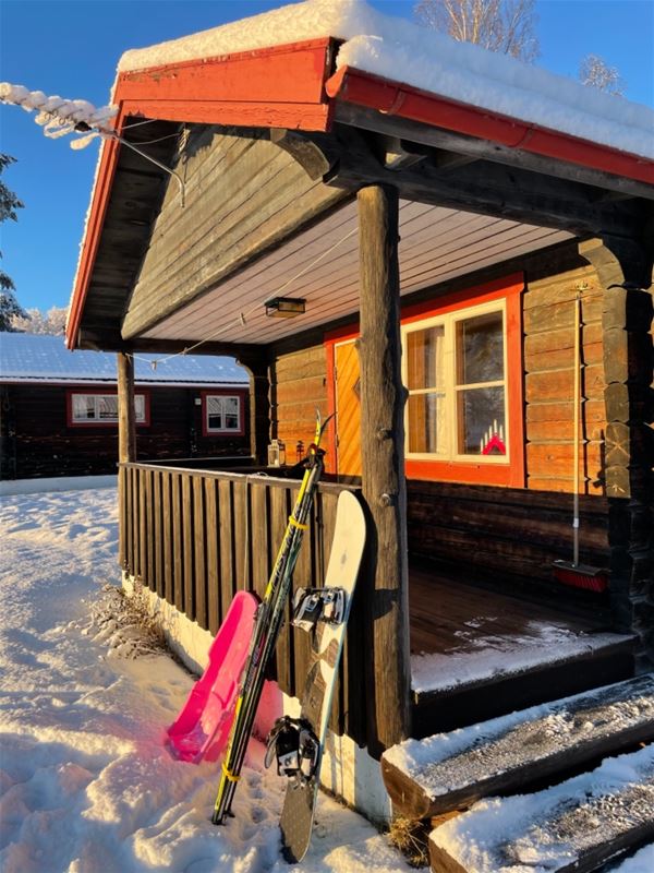 Pulka, längdskidor och snowboard lutar mot altanen på en stuga.